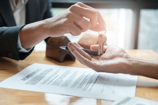 estate agent giving house keys to man and sign agreement in office